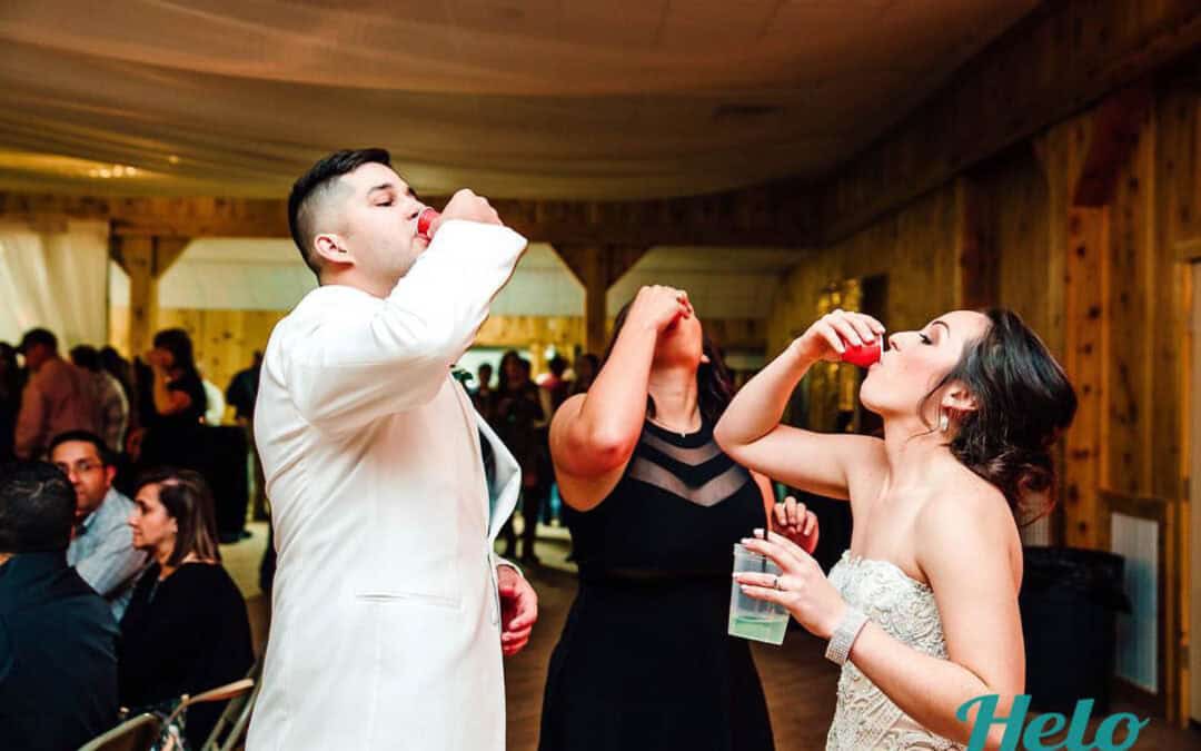 Three people taking shots at an indoor event, with others seated in the background.