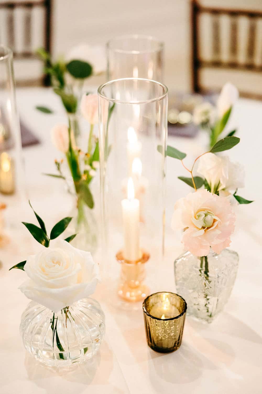 Candles and white flowers in glass vases arranged on a table with a neutral tablecloth.